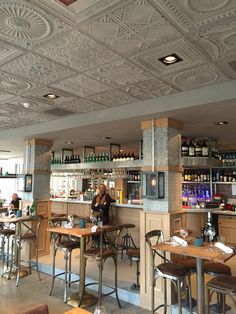 an empty restaurant with tables and stools in front of the bar, while people are seated at the counter