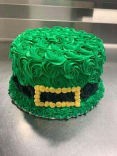 a cake with green frosting and yellow icing on it's face is sitting on a table