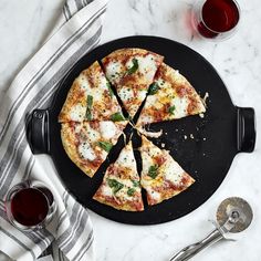 a pizza sitting on top of a black plate next to two glasses of red wine