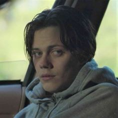 a man sitting in the back seat of a car wearing a hoodie and looking off into the distance