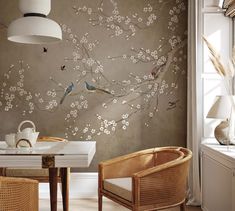 two chairs and a table in front of a wall with birds on it's branches