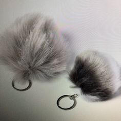 two furry balls are attached to a pair of metal hoop earrings on a white surface