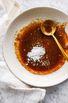 a white bowl filled with sauce and powdered sugar next to a spoon on top of a towel