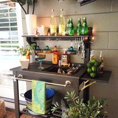 an outdoor bar with bottles and glasses on the shelf next to potted plants in front of it