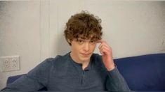 a young man sitting on top of a blue couch holding his hand to his head