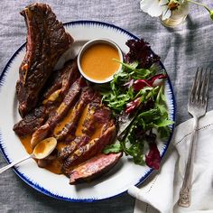 a white plate topped with steak and salad next to a fork, knife and spoon