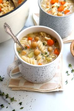 two bowls filled with pasta and carrots on top of a white tablecloth next to a pot full of soup