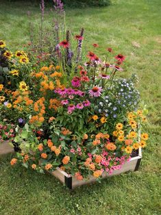 a wooden box filled with lots of colorful flowers on top of green grass covered ground