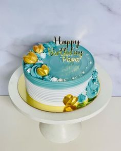 a birthday cake with blue frosting and gold flowers on the top is sitting on a white pedestal