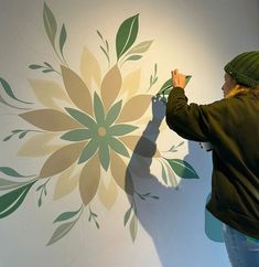 a woman painting a flower on the wall with green and yellow flowers painted on it