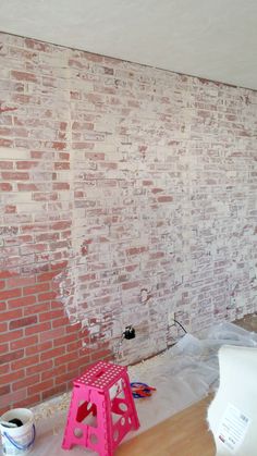 a brick wall is being painted with white paint and pink stools on the floor