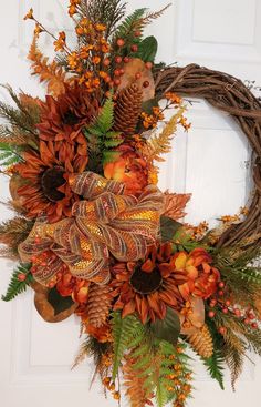 a wreath with orange flowers and pine cones is hanging on the front door's white door