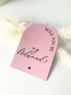 a piece of pink paper with the words will you be my bridesmaid written on it