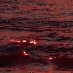 the sun is setting over the ocean with red lights in the water and some waves