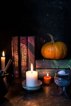 candles and books on a table in front of a pumpkin