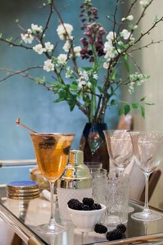 there is a glass table with wine glasses and berries on the plate next to it