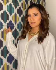 a woman is standing in front of a wall with colorful tiles and gold chains on it