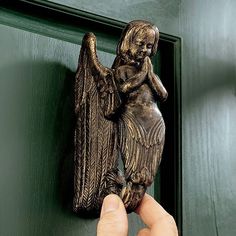 a person holding an angel figurine in front of a green door with black trim