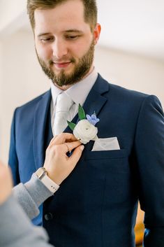 a man in a suit adjusts his boutonniere