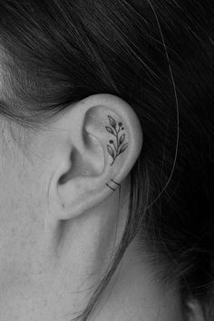 a woman's ear with a small leaf tattoo on it