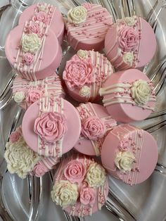 pink and white cupcakes with roses on them sitting on a silver platter