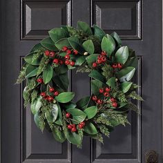 a wreath with red berries and green leaves hangs on the front door's black doors