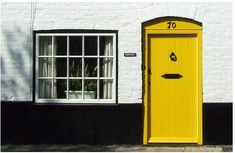 a yellow door is in front of a white house with black windows and shutters