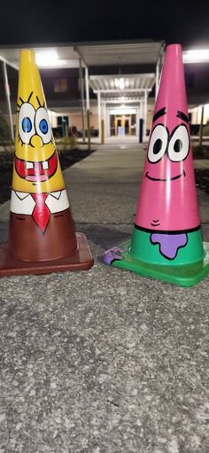 two plastic cones with faces on them sitting in the middle of a sidewalk at night