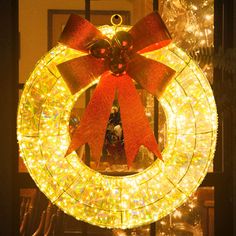 a lighted wreath with a red bow hanging from it's center and surrounded by christmas lights