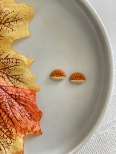 two cookies sitting on top of a white plate next to an orange and yellow leaf