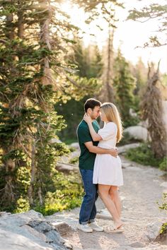 a man and woman embracing each other while standing on a rock in front of trees