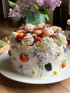 a cake with flowers and berries on it sitting on a plate next to a vase