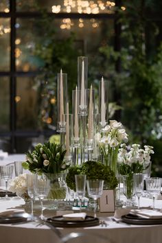 the table is set with clear vases and greenery for an elegant wedding reception