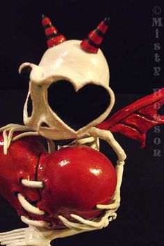 a skeleton holding two red apples with horns and hearts on it's back, in front of a black background