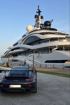 a black sports car parked in front of a large yacht