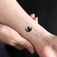 two hands holding each other with a small tattoo on the wrist that has a black cat in it