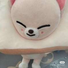 a white stuffed animal with pink ears and eyes sitting on top of a pillow in the shape of a bear