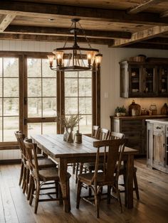 a dining room table surrounded by chairs in front of two large windows with wooden beams