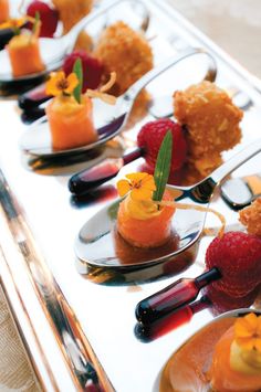 small desserts are arranged on spoons with flowers and fruit garnishes