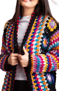 a woman wearing a multicolored crocheted cardigan and smiling at the camera