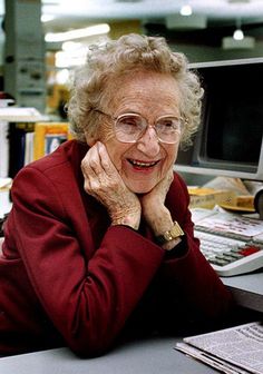 an older woman sitting at a desk with a computer monitor and keyboard in front of her