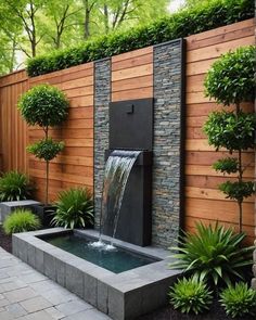 a water fountain in the middle of a garden with trees and plants around it, surrounded by wooden fence