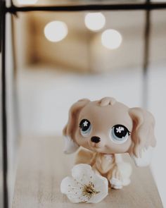 a little dog figurine sitting on top of a wooden table next to a flower