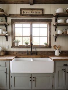 a white kitchen sink sitting under a window next to wooden shelves filled with pots and pans