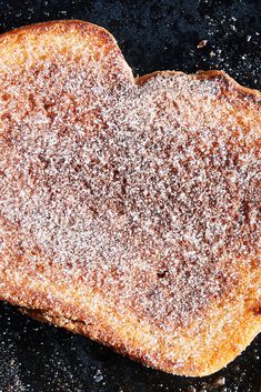 a heart shaped piece of bread covered in powdered sugar on top of a black surface