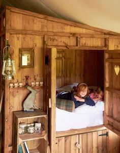 two children laying on a bed in a room with wood paneled walls and flooring