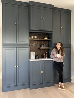 a woman sitting on the kitchen counter in front of some cupboards holding a cup