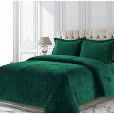 a bed with green comforter and pillows in a white room next to a lamp