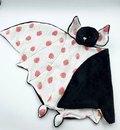 a black cat laying on top of a white table next to a pink strawberry blanket