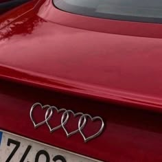 three hearts are attached to the tail end of a red car with chrome lettering on it